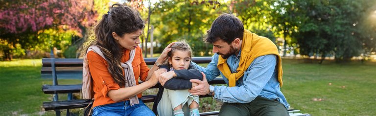 On a bench in a park a mother and father comfort their child when the world feels unsafe